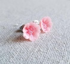 two pink flower earrings sitting on top of a gray cloth covered table next to a pair of scissors