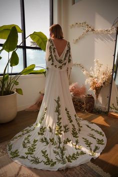 a woman standing in front of a window wearing a white dress with green leaves on it