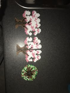 a cross - stitch pattern on a black surface with pink flowers and a green object