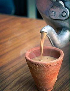 a clay cup filled with liquid sitting on top of a wooden table next to an animal statue