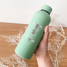 a person holding a green water bottle on top of a wooden table with white branches