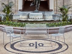 two chairs and a table in front of a fountain with a statue on it's side