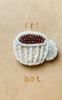 a brooch with beads in the shape of a coffee cup on top of a piece of paper