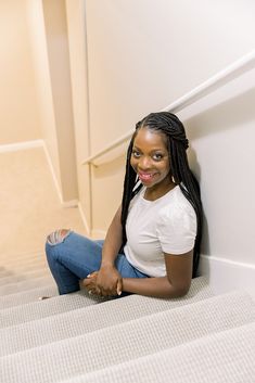 a woman is sitting on the stairs with her hand in her pocket and smiling at the camera