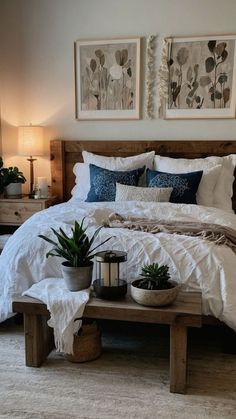 a bed with white linens and blue pillows in a small room next to two planters