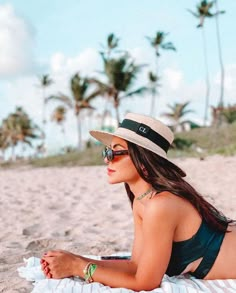 a woman laying on top of a beach wearing a hat and sun glasses with palm trees in the background