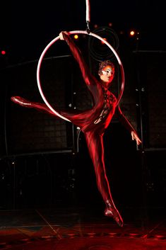 a woman is doing aerial tricks with a hoop on her back while standing in the dark