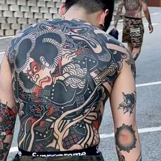 a man with lots of tattoos on his back walking down the street next to another person