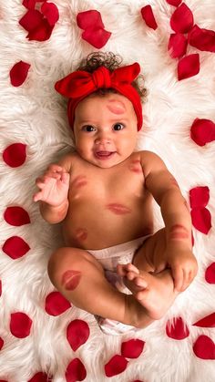 a baby is sitting on a white rug with red petals around it and smiling at the camera