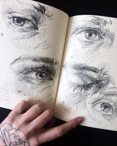 a person's hand holding an open book with drawings on the pages and in front of them