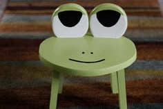 a little green chair with two eyes on it's face and one in the shape of a frog