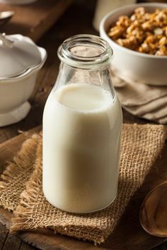 a glass bottle filled with milk sitting on top of a table next to bowls and spoons