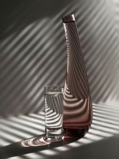 a vase and glass sitting on a table with the shadow cast by it's side