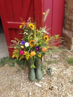 a bouquet of flowers in green rubber boots sitting on the ground next to a red door