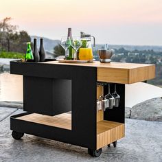 an outdoor bar cart with drinks and glasses on the table, overlooking a body of water