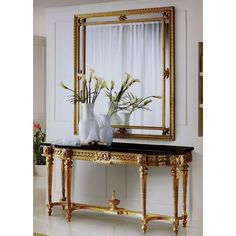 two vases with flowers sit on a table in front of a large gold framed mirror