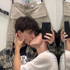 a man and woman kissing in front of a mirror while looking at their cell phones