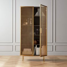 an open cabinet with books and other items in it on a wooden floor next to a white wall