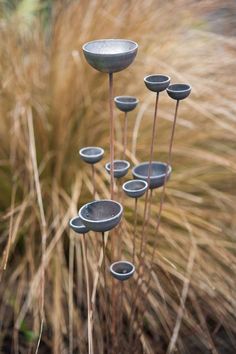 a group of metal vases sitting on top of a grass covered field next to tall dry grass