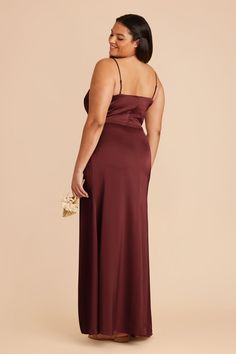 a woman in a long burgundy dress is smiling and looking away from the camera with her hand on her hip