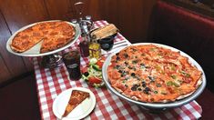 two large pizzas sitting on top of a table next to plates of food and condiments