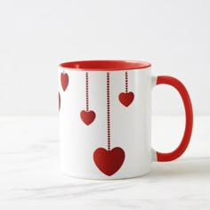 a red and white coffee mug with hearts hanging from it