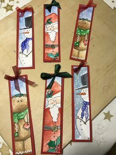 four christmas bookmarks with santa and snowmen on them, hanging from ribbon ties