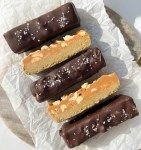 five chocolate covered donuts sitting on top of a white paper towel next to a knife and fork