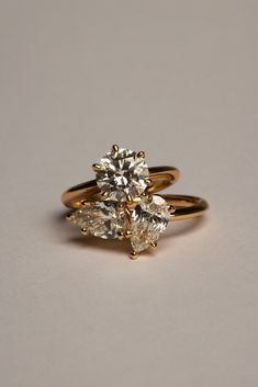 two gold engagement rings with three pear shaped diamonds on each one, set against a plain background