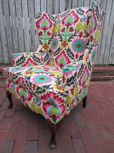 a colorful chair sitting on top of a brick floor next to a wooden fence in the back yard