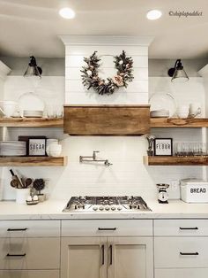 a white kitchen with open shelving above the stove and shelves on the wall, decorated with wreaths