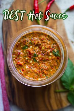 a glass jar filled with food sitting on top of a wooden cutting board next to peppers