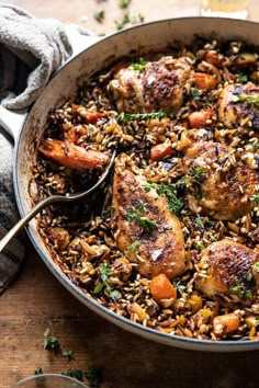 a pan filled with chicken and rice on top of a wooden table next to a glass of wine