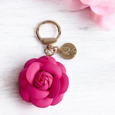 a pink rose keychain sitting on top of a white table next to flowers