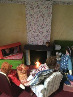 three dolls sitting in chairs around a fire place