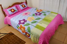 a bed with pink and green bedspread on top of it next to a window