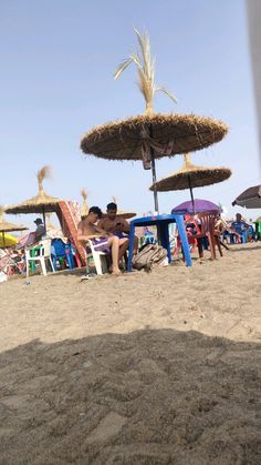 two men sitting under umbrellas on the beach