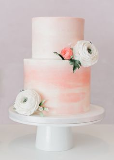 a pink and white wedding cake with flowers on top