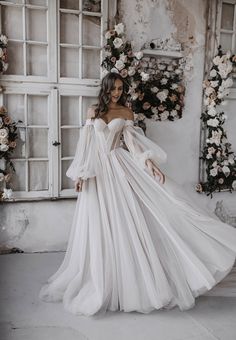 a woman in a white wedding dress with long sleeves and flowing ruffles on the skirt