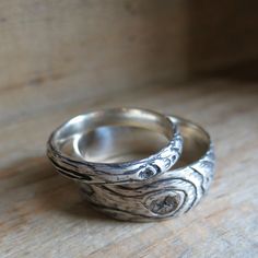 two silver rings sitting on top of a wooden table next to each other and one has a tree branch engraved on it