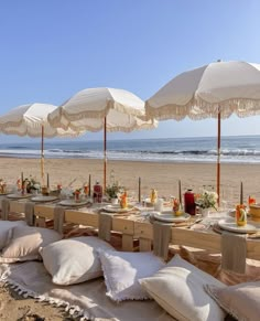 an outdoor table set up on the beach with white umbrellas over it and food