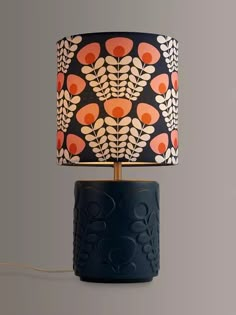 a lamp with an orange and black design on the shade is sitting next to a gray wall