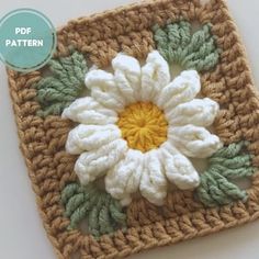 a crocheted square with a white flower on the center and green leaves around it