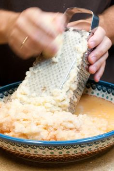 a person grating mashed potatoes into a bowl with a grater in it