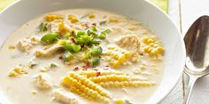 a white bowl filled with soup and corn on the cob next to a spoon