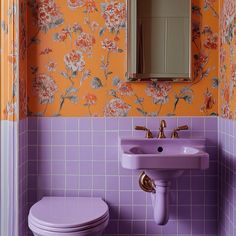 a purple sink and toilet in a bathroom with orange wall paper on the walls behind it