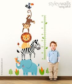 a little boy standing next to a growth chart with animals on it and a monkey