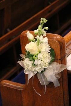 a bouquet of white flowers sitting on top of a wooden chair in front of a pew