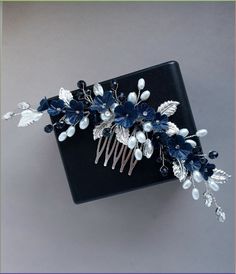 a hair comb with flowers and leaves on top of a black box against a gray background