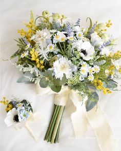 a bouquet of white and blue flowers with green leaves on a white sheet next to it